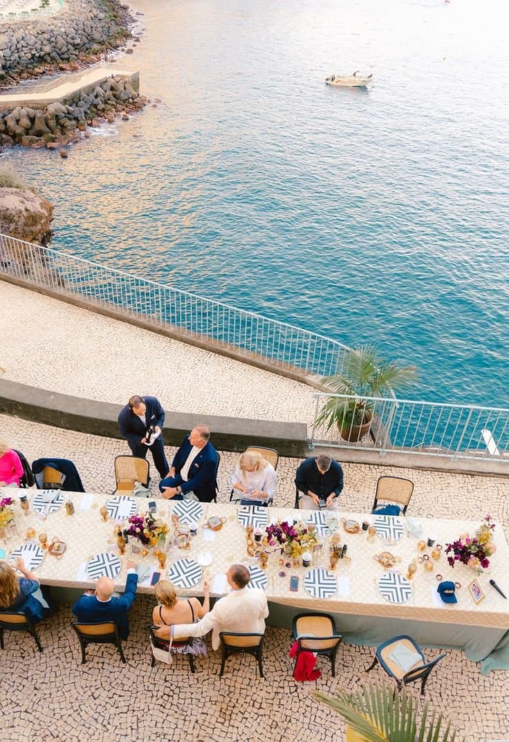 Guests at a long dinner table on a waterfront terrace